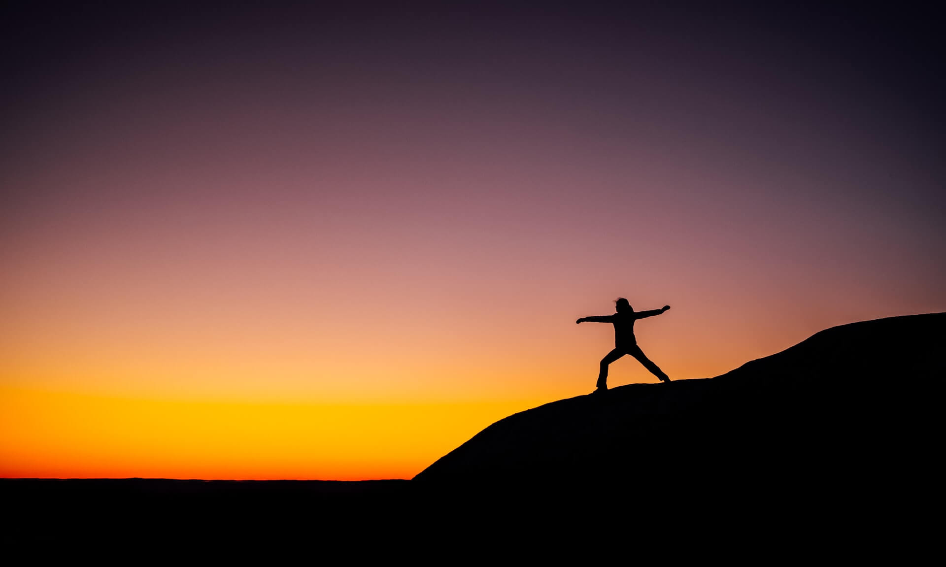 The silhouette of a human doing yoga during sunset.